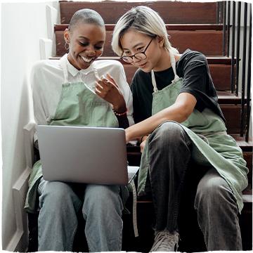 Dvě ženy sedící na schodech s laptopem