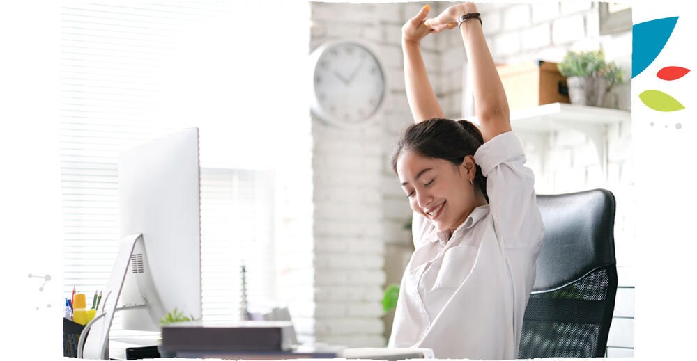 Usmívající se žena, která natahuje ruce vzhůru, má chvíli úlevy při práci na počítači.