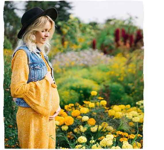 Těhotná žena odpočívá v parku plném květin