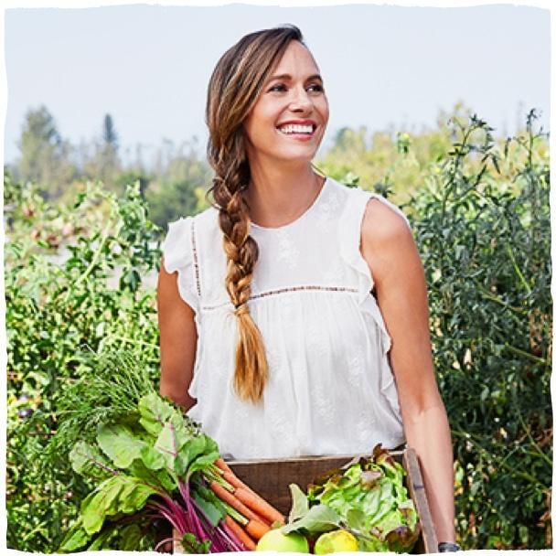 Žena s copem na poli drží bendu se zeleninou